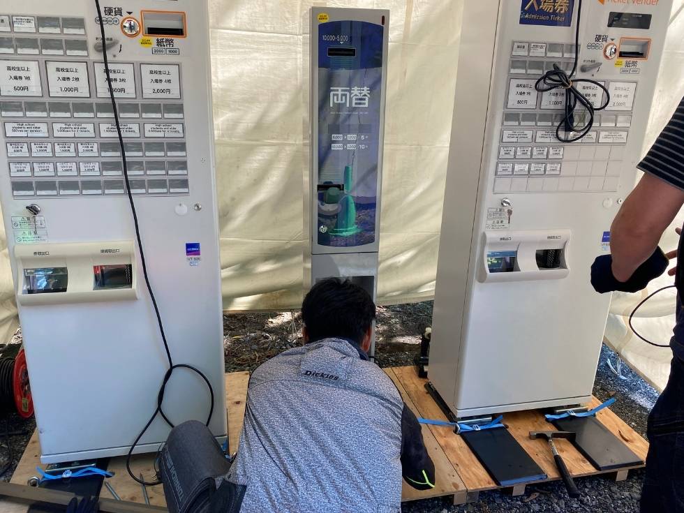 アトラスのスタッフが水平が取れてない地面に券売機を設置する作業風景